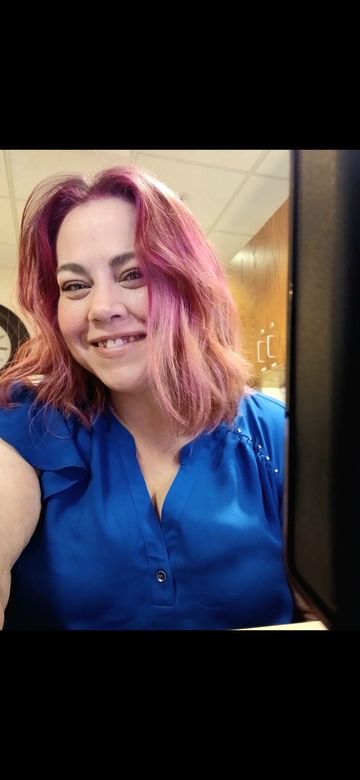 Heather Dyer smiling, with pink hair and a blue blouse